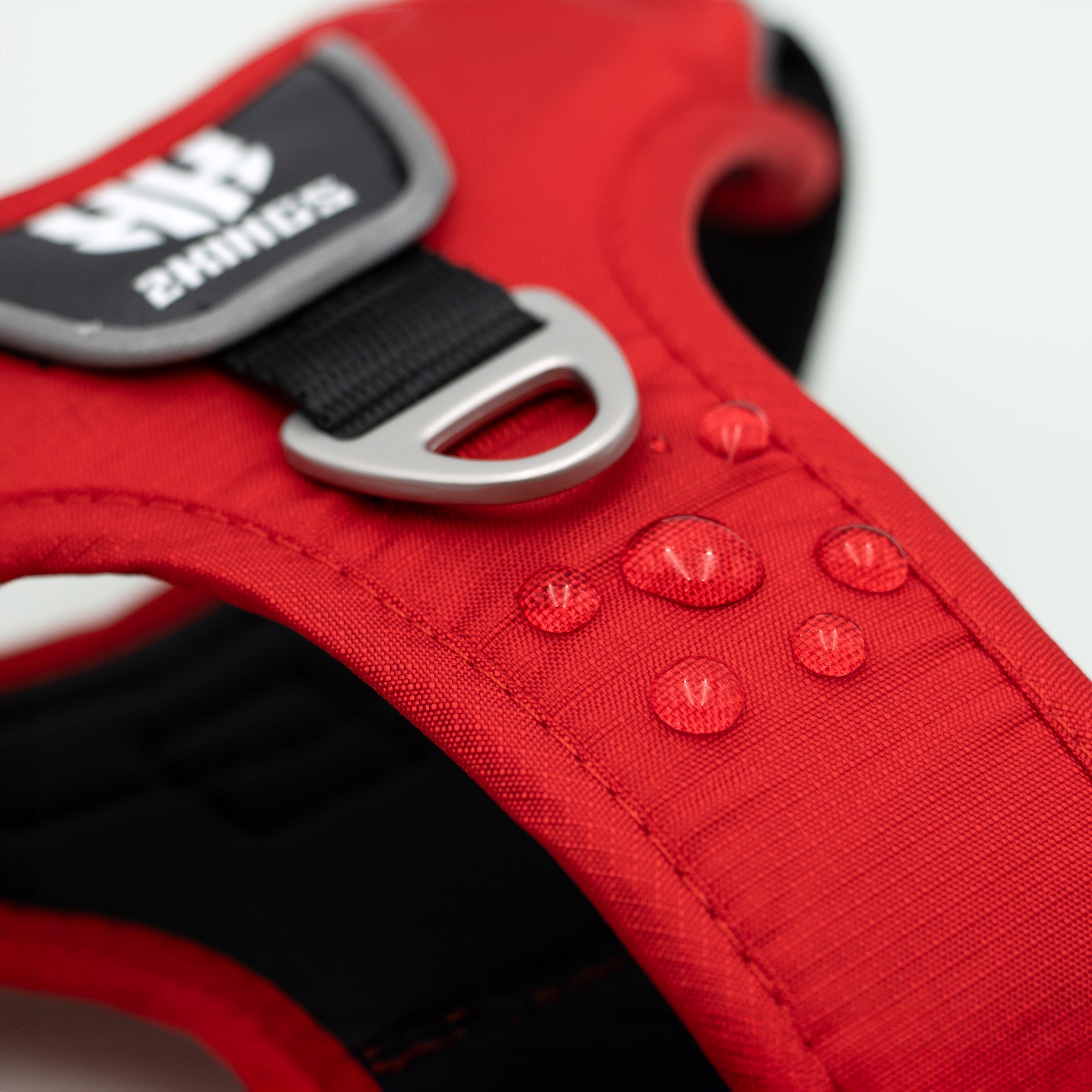 Red comfort dog harness highlighted by water droplets to showcase its waterproof feature, designed for durability and comfort in wet conditions.